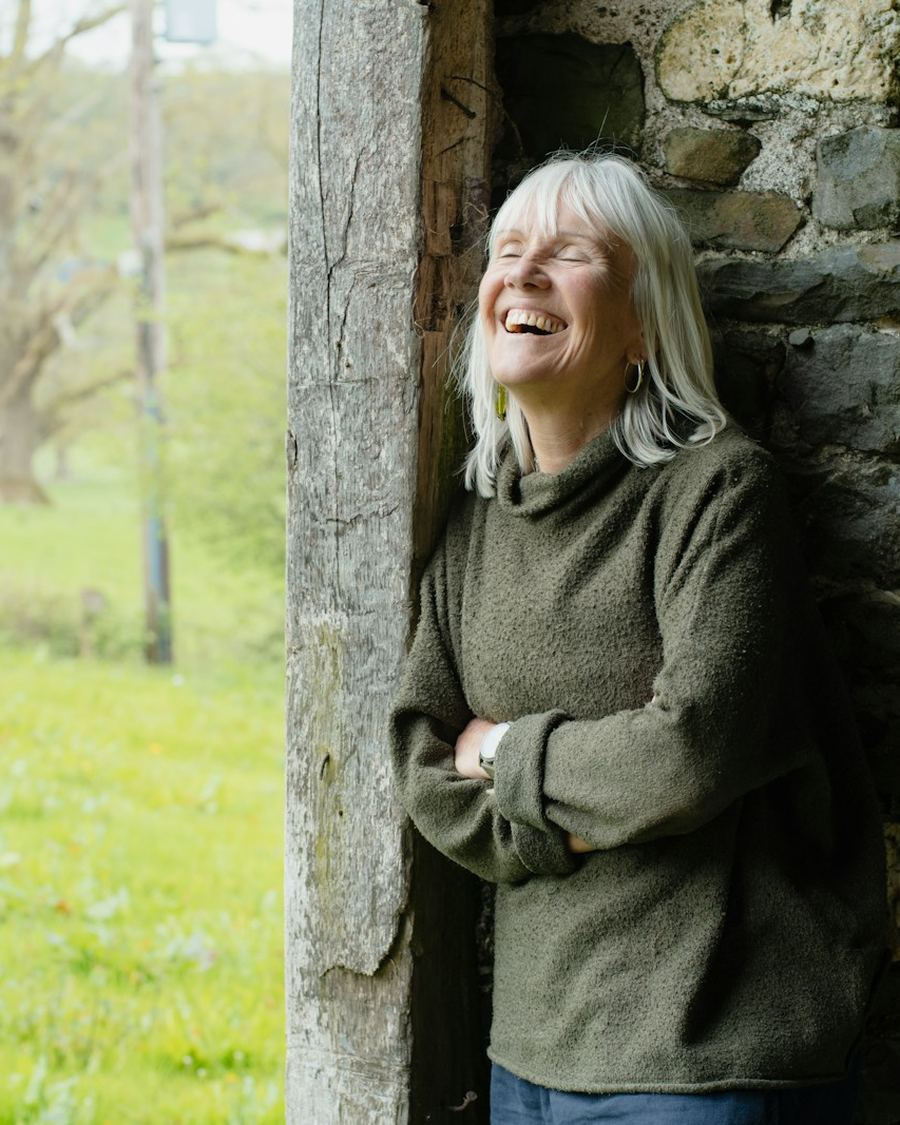 Smiling woman with grey hair leaning in a sunlit doorway